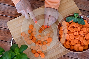 Wooden cutting board and female hands cutting fresh carrots in round shape - healthy, diet, vegetables concept