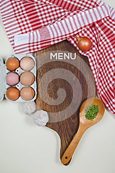 Wooden cutting board with food spices, spoon, eggs and garlics