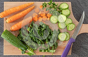 Wooden cutting board with fresh organic vegetables and knife, top view, close-up