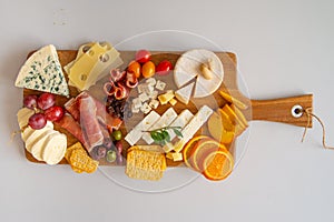 A wooden cutting board full of different types of cheese, bacon, and a few fruits. Overhead view. isolated on white