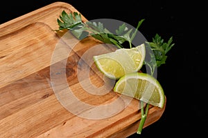 Wooden cutting board with greens and lime on a black background