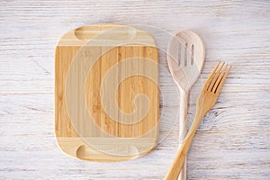 Wooden cutting board and kitchenware on wooden background, space for text, flat lay