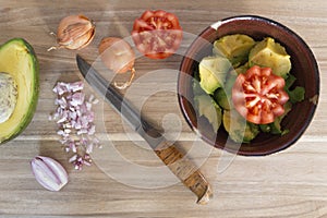 Wooden cutting board with knife, fresh onions, tomato and avocado