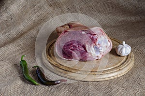 Wooden cutting board with pork leg, head of garlic and hot pepper pods