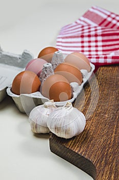 Wooden cutting board with red rug, spices, ladle, eggs and garlics