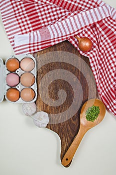 Wooden cutting board with red rug, spices, ladle, eggs and garlics