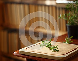 Wooden cutting board with rosemary near, books on background, home cozy interior