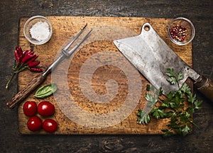 Wooden cutting board with Slasher meat fork meat pepper salt tomatoes, fresh herb top view rustic wooden background photo