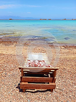 Wooden deck chair and cushion and turquoise waters of the Red Sea in the Sinai Peninsula. Back view of empty sun lounger. Chill