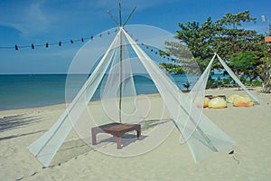 Wooden deck chair in white pavilion on sand beach with beautiful seascape view and blue sky in background.