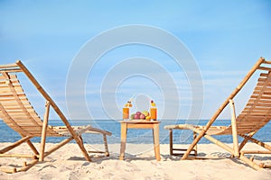 Deck chairs near table with fruits and drinks on beach