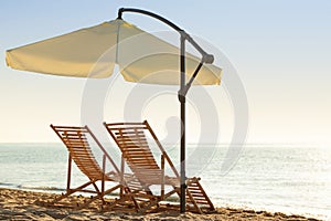 Wooden deck chairs and outdoor umbrella on sandy beach. Summer vacation