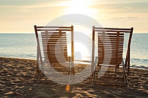 Wooden deck chairs on sandy beach at sunset. Summer vacation