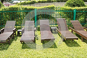 Wooden deck chairs stand in a row on the green grass under the sun in the recreation area on the private territory of a modern