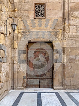 Wooden decorated copper plated door and stone bricks wall at the courtyard of Al-Sultan Barquq mosque, Old Cairo, Egypt