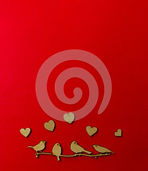 Wooden decoration flock of enamored birds sitting on a branch and wooden hearts around birds on a red background. Copy space.