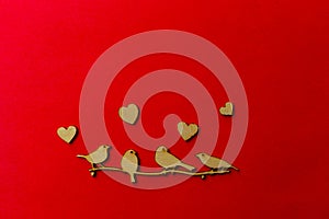 Wooden decoration flock of enamored birds sitting on a branch and wooden hearts around birds on a red background. Copy space.