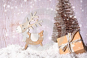 Wooden deer on a sled and a box with a gift close-up on a background of a golden Christmas tree, front view.