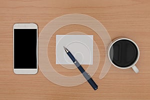 Wooden desk with blank smart phone, coffee, paper note and pen