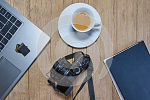 Wooden desk table with camera, laptop, memory cards, espresso cup and clipboard.