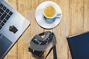 Wooden desk table with camera, laptop, memory cards, espresso cup and clipboard.