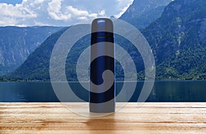 Wooden desk with thermos and landscape on background