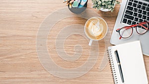 Wooden desk workplace with laptop computer, notebook, eyeglass, pen and cup of coffee