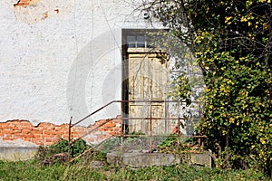 Wooden dilapidated entrance doors to abandoned ruins of suburban family house with broken steps and rusted metal fence