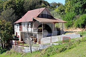 Wooden dilapidated old family house with large front porch and new roof tiles built on side of small hill