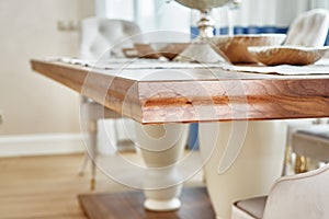 Wooden dinner table on massive legs with dishware in modern apartment. Close-up