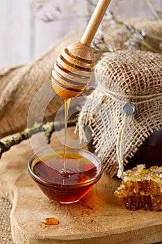 Wooden dipper with flowing fresh natural honey. Fresh harvesting brown forest honey in glass bowl and jar. Healthy dessert