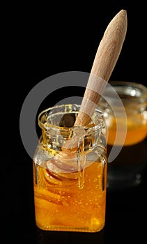 Wooden dipper in jar with honey against dark background