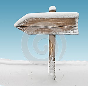 Wooden direction sign with snow on it with sky on background