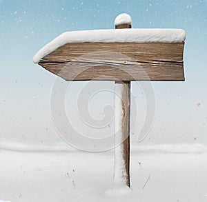 Wooden direction sign with less snow with snowfall on background