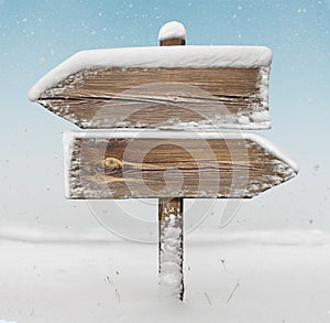 Wooden direction sign with snow and snowfall bg. two_arrows-opposite_directions