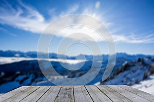 Wooden display shelf table top against blurred snow covered winter mountain panorama on a sunny day, blue sky