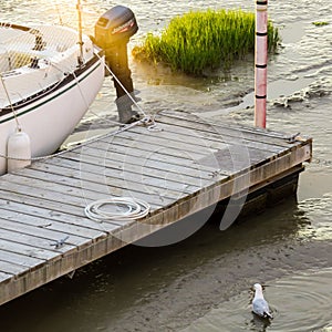 Wooden dock with a boat parked next to it and a white bird in the water.