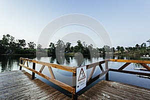 Wooden dock with a [Perigo - danger] sign on a lake under a blue sky and sunlight at daytime photo