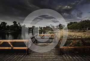 Wooden dock with a [Perigo - danger] sign on a lake under a dark cloudy sky in the evening