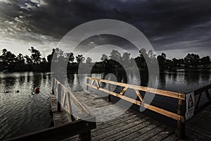 Wooden dock with a [Perigo - danger] sign on a lake under a dark cloudy sky in the evening photo