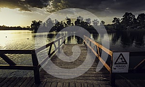 Wooden dock with a [Perigo - danger] sign on a river under a dark cloudy sky in the evening photo