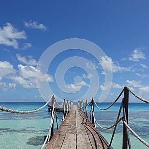 A wooden dock with ropes leads out into a tropical lagoon with coral on the island of Fakarava in French Polynesia