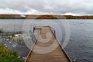 Wooden dock on the Superior lake surrounded by yellowing trees on a gloomy day in autumn in Michigan