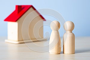 Wooden doll couple stands in front of house model. Family together protection and home insurance concept
