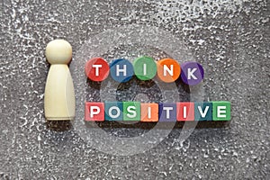 Wooden doll beside the THINK POSITIVE text on the colorful wooden blocks lifestyle concept