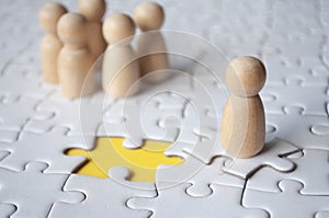 Wooden doll on top of jigsaw with missing jigsaw puzzle. Hiring and employment concept