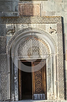 Wooden door, covered with a carved ethnic ornament, and a stone oval plane with carved fruit patterns above the doorway church of