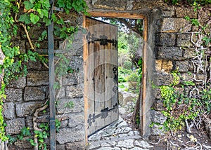 Wooden door decorated with iron forging, slightly open. Wall of