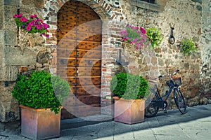 Wooden door with flowery entrance and retro bicycle, Pienza, Tuscany