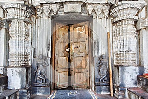 Wooden door in historical Hindu temple with stone walls, collumns, carvings and sculptures, India.